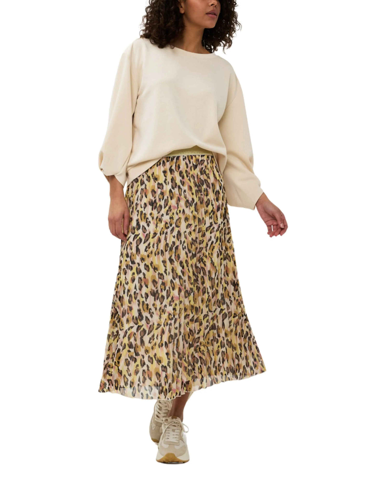 Mujer con falda midi plisada de estampado animal y blusa beige, look casual moderno.