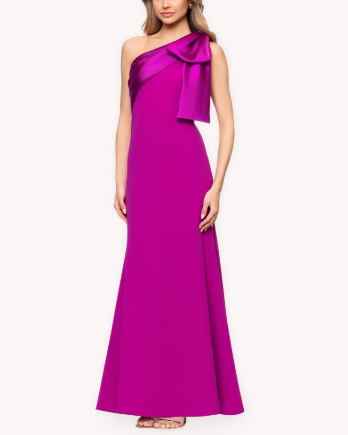 Vestido largo un hombro con moño vista frontal completa en fucsia con silueta entallada