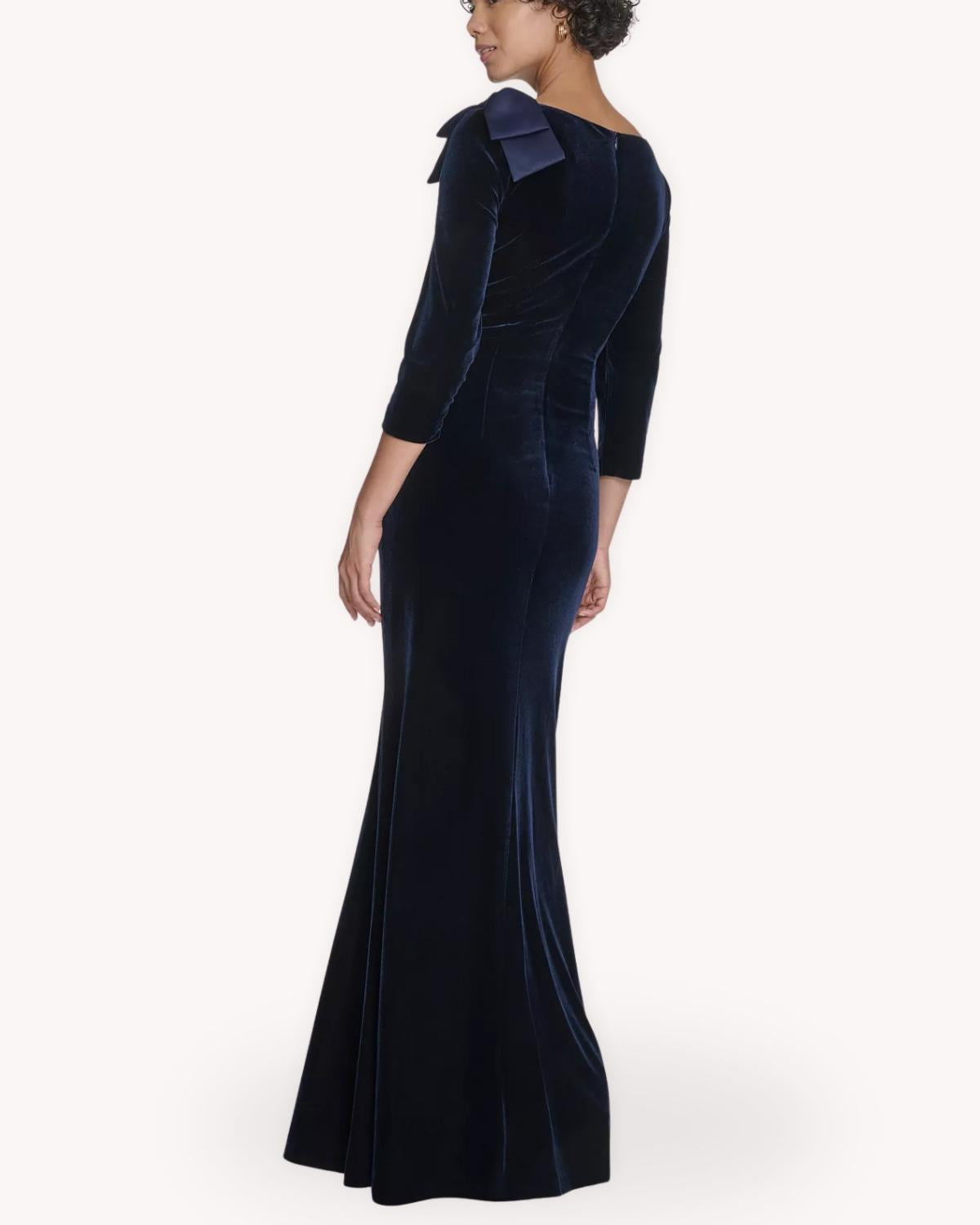 Vista posterior del vestido largo de terciopelo azul marino con moño en hombro y falda ligeramente evasé